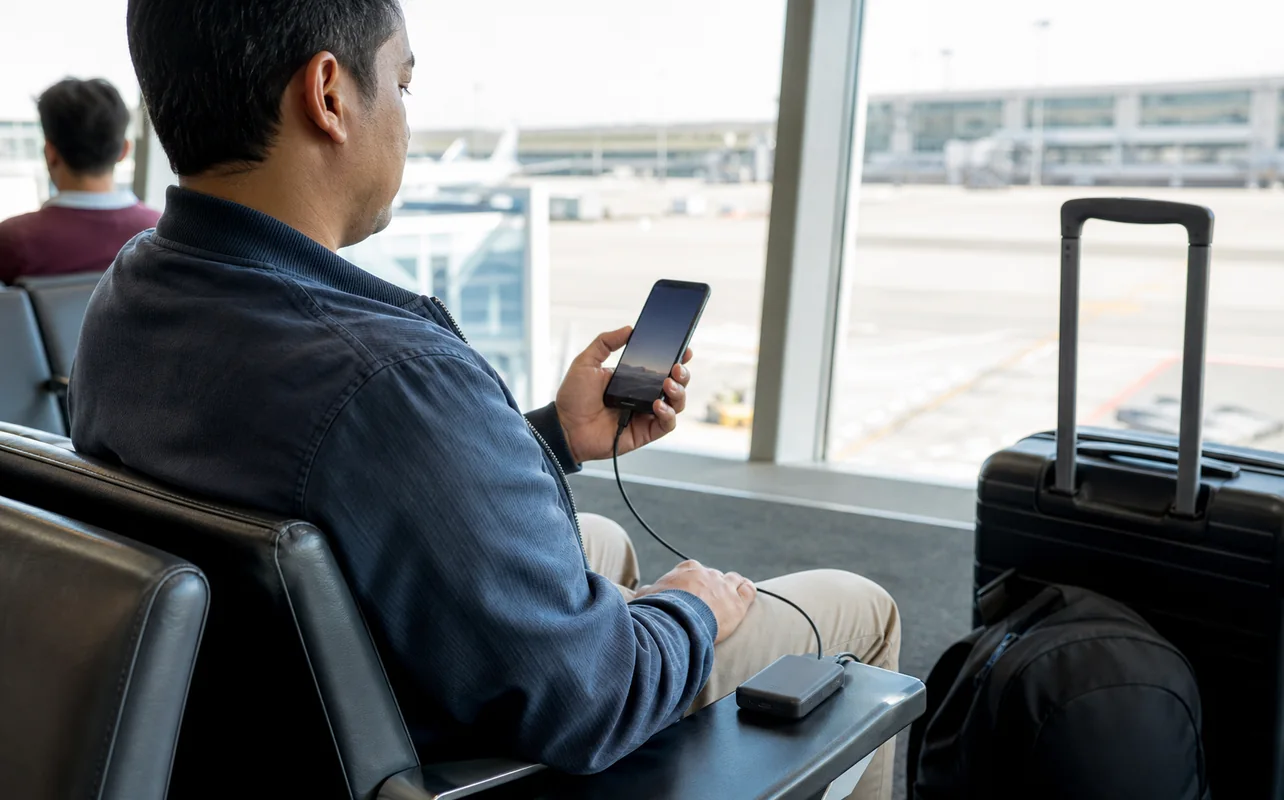 A realistic everyday scene illustrating a traveller charging a phone from a compact power bank at an airport gate